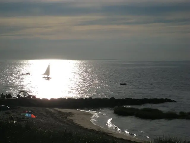 This picture is taken on a sea shore. On the shore, there are people and umbrellas. On the ocean,...